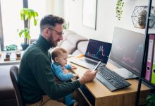 Person with baby looking at financial performance on computer in home office.