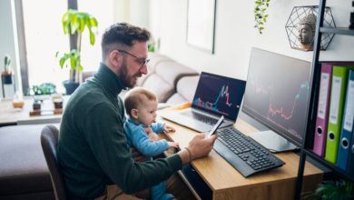 Person with baby looking at financial performance on computer in home office.