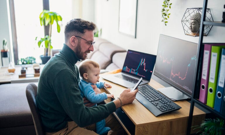 Person with baby looking at financial performance on computer in home office.